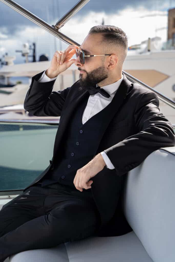Omid Farahani seated on a boat wearing a black suit and sunglasses