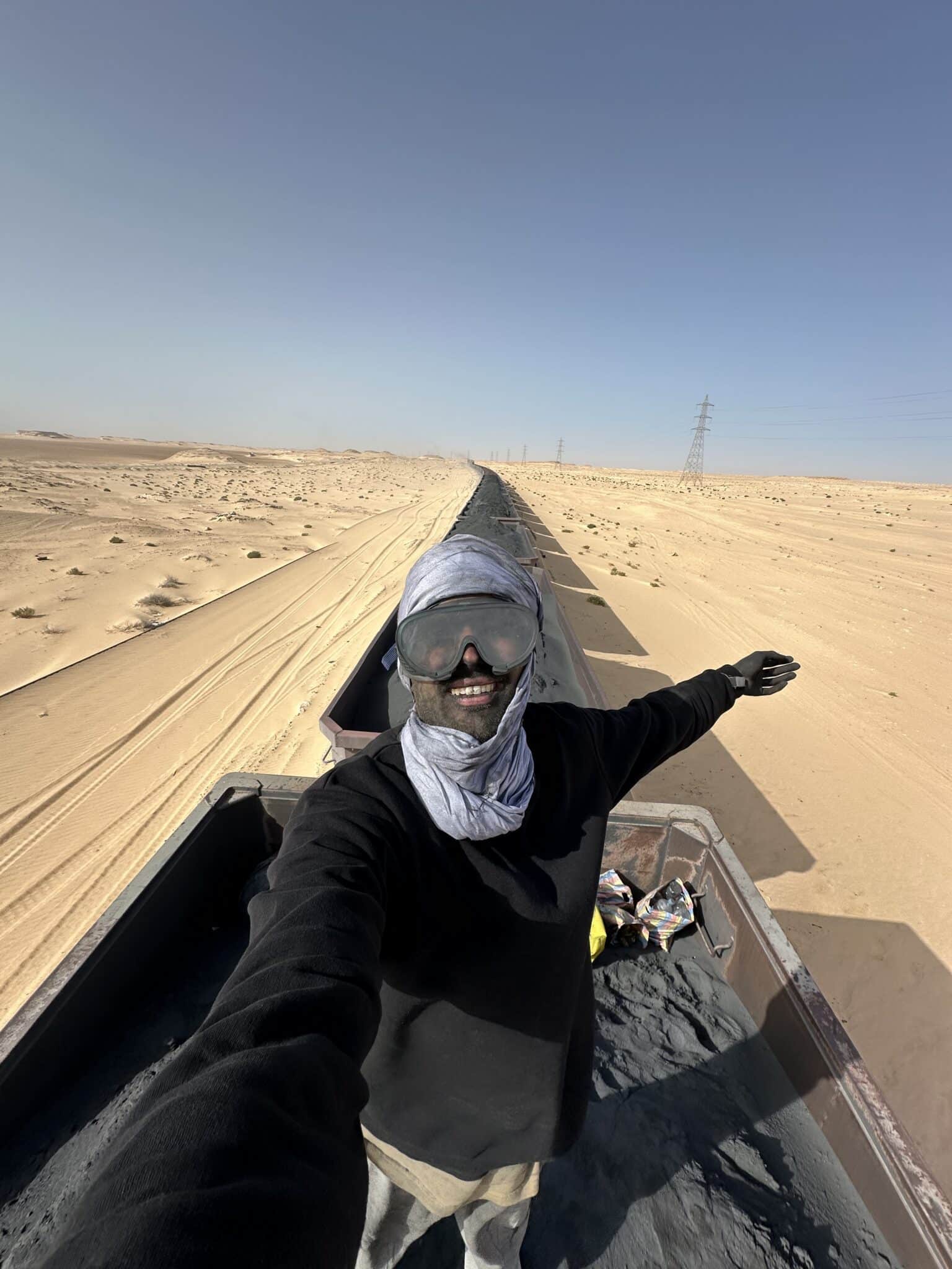 Jesper Hedlund taking a selfie on a long freight train in the desert, wearing goggles and a head covering.